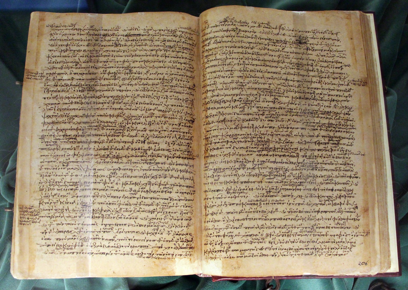 An open Greek manuscript with dense brown handwriting and marginal notes, displayed on green cloth.