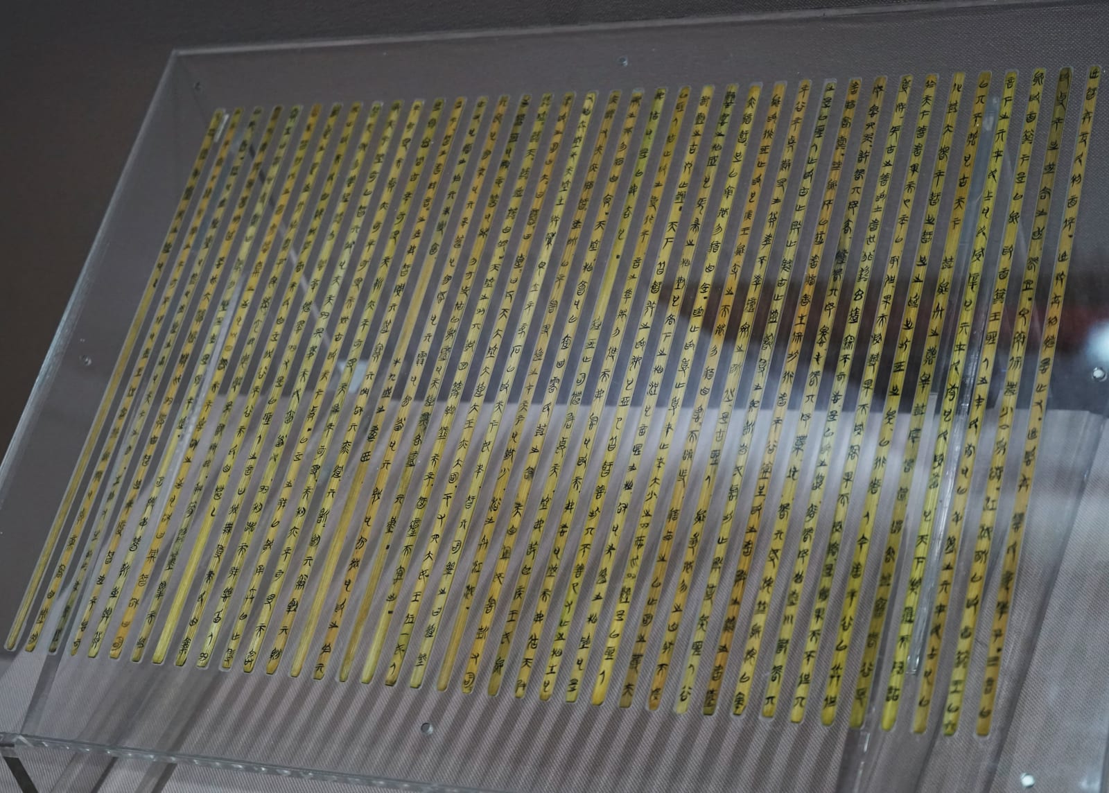 Rows of narrow bamboo slips covered in ink characters, displayed on a sloping clear stand.