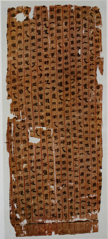 A worn strip of silk ruled with red lines and written in columns of black Han clerical script.