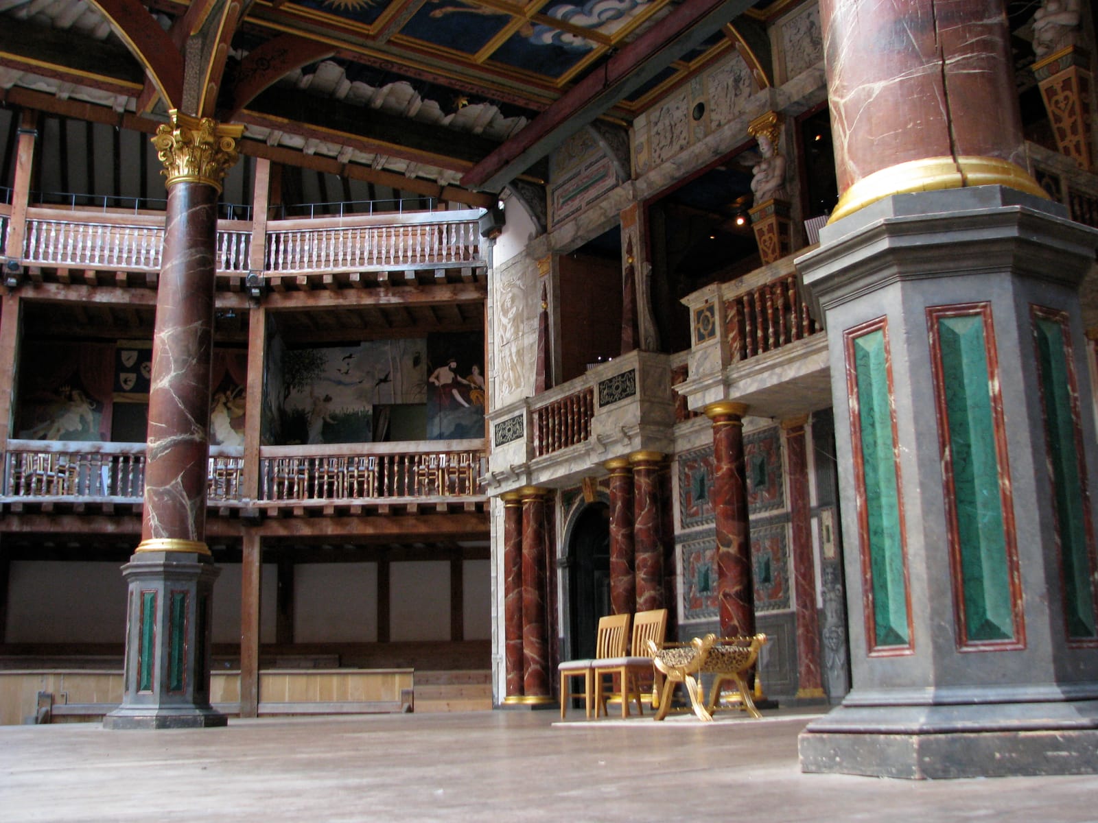 The stage of the reconstructed Globe seen from the standing yard: painted pillars, a richly decorated back wall with doors, and wooden galleries.