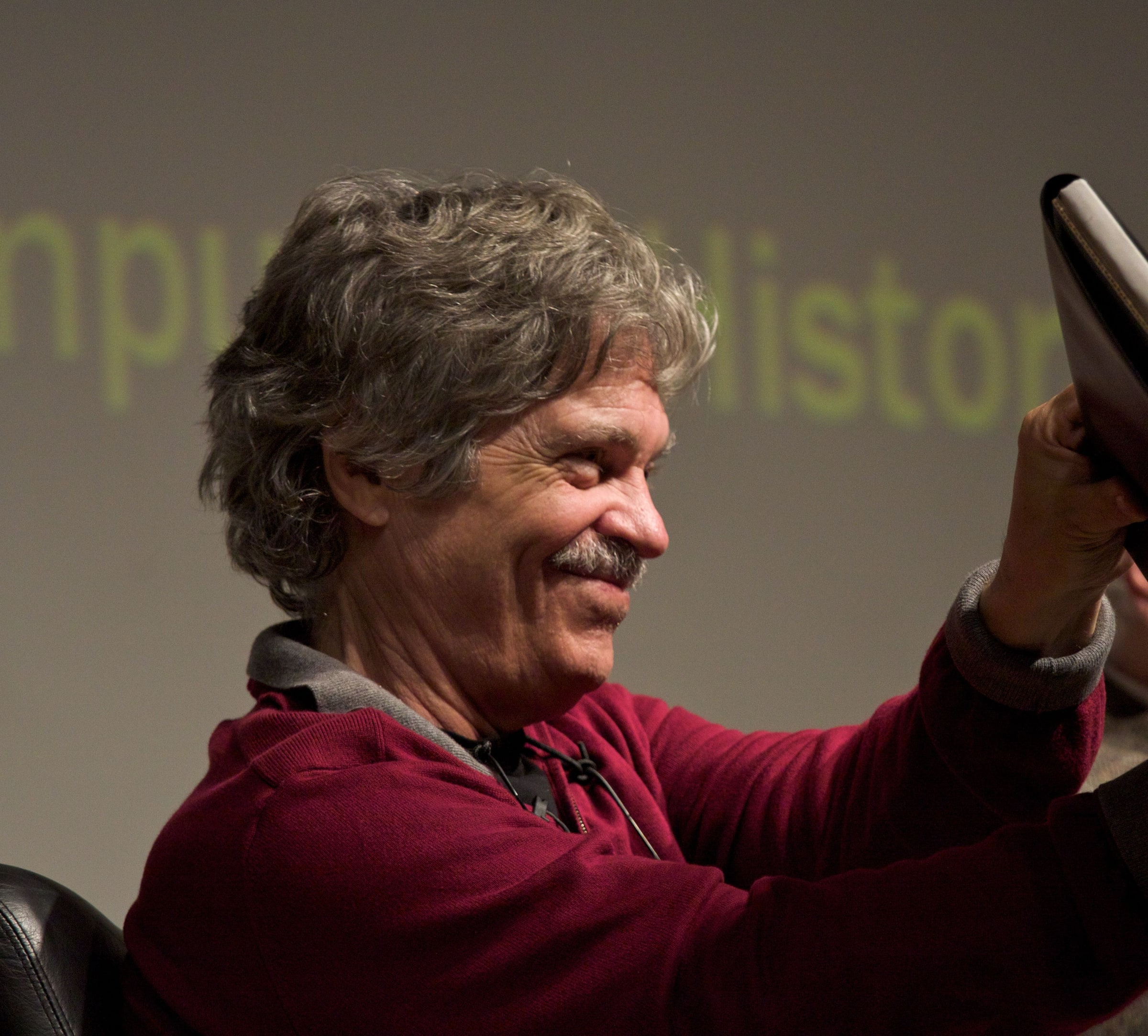 Alan Kay smiling as he lifts the Dynabook prototype at the Computer History Museum, November 2008.