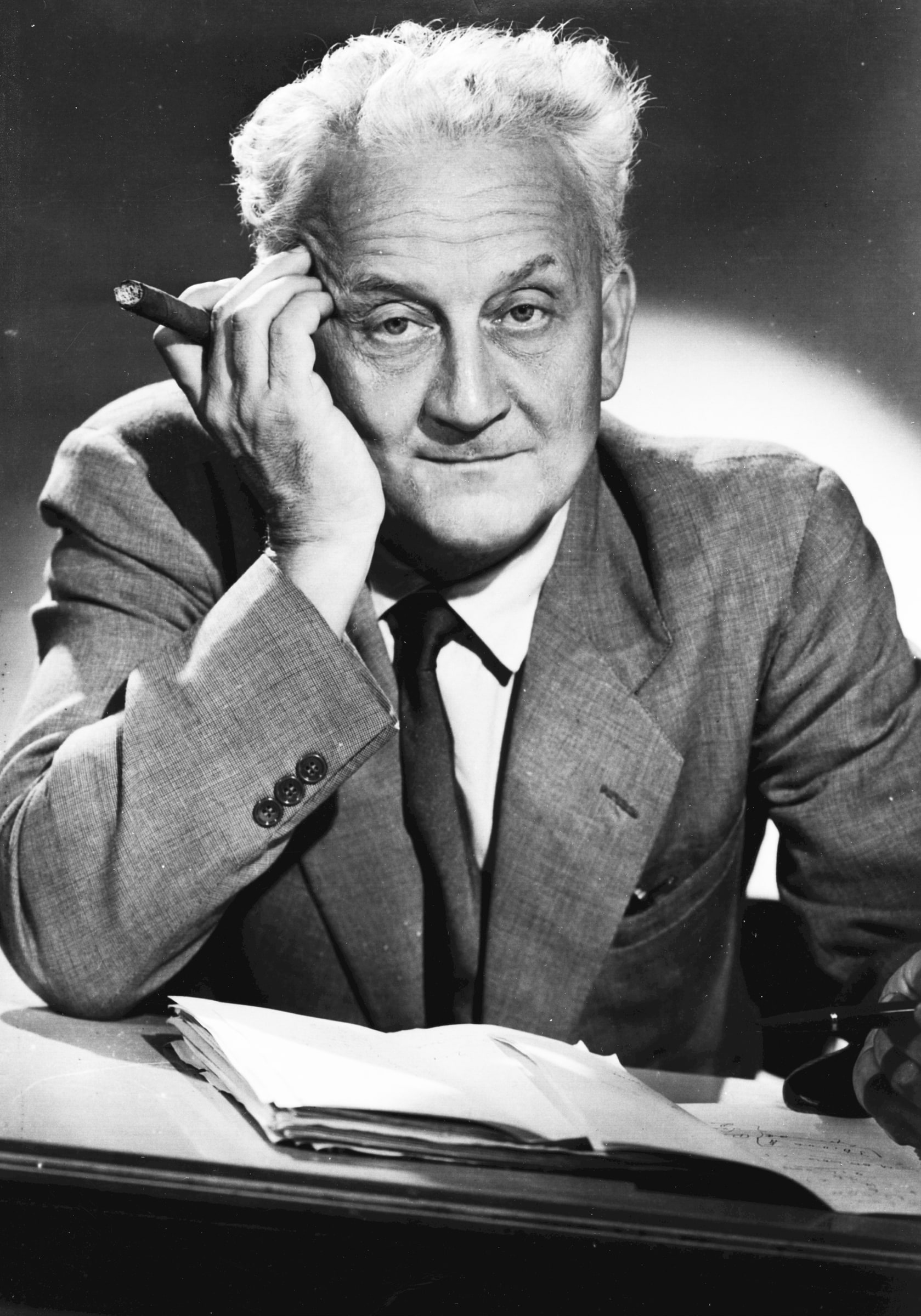 Albert Szent-Györgyi in 1950, cigar in hand and head resting on his fingers, seated at a desk of papers.
